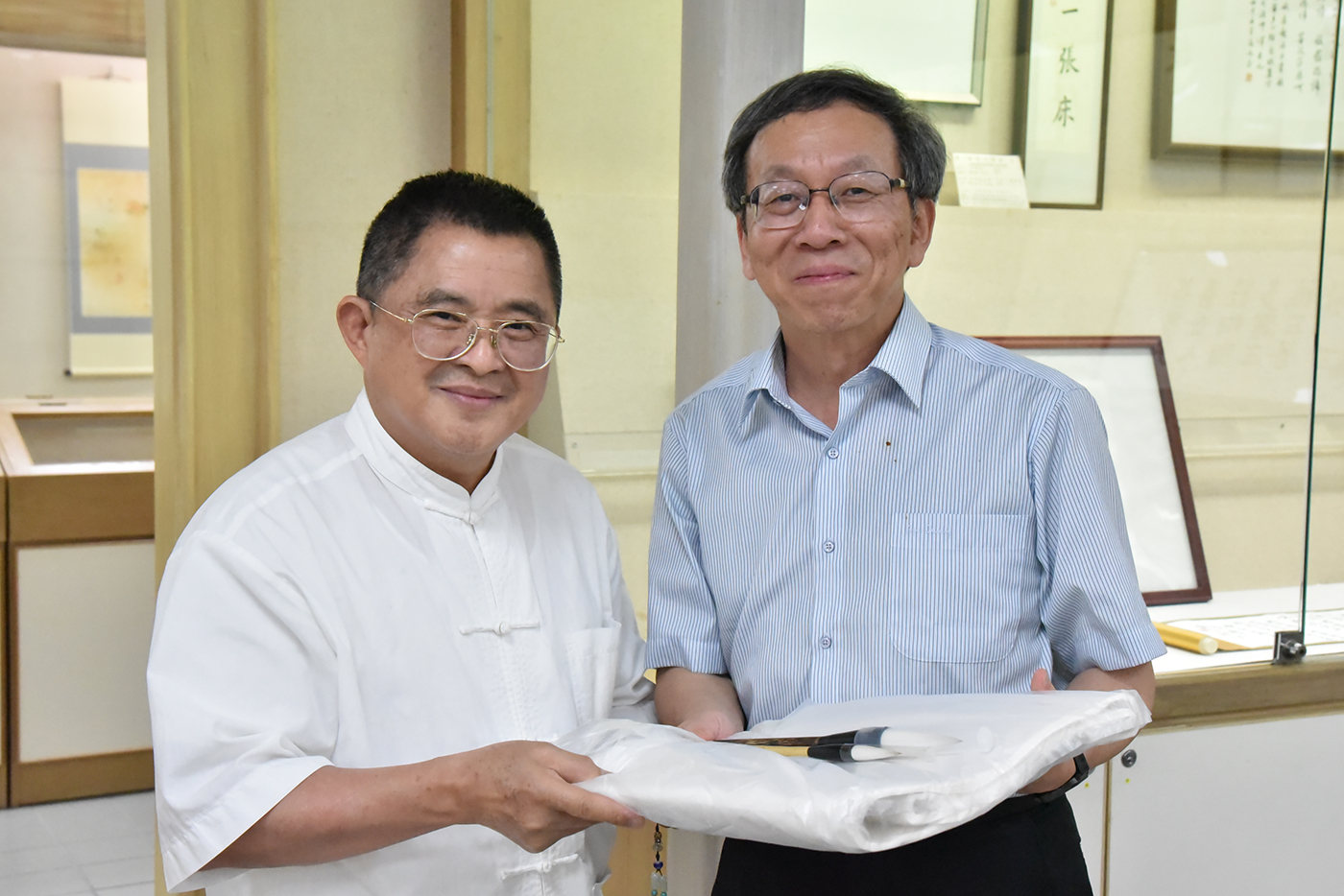 策展人吳大仁老師（左）致贈簡江儒教務長兩支毛筆。 